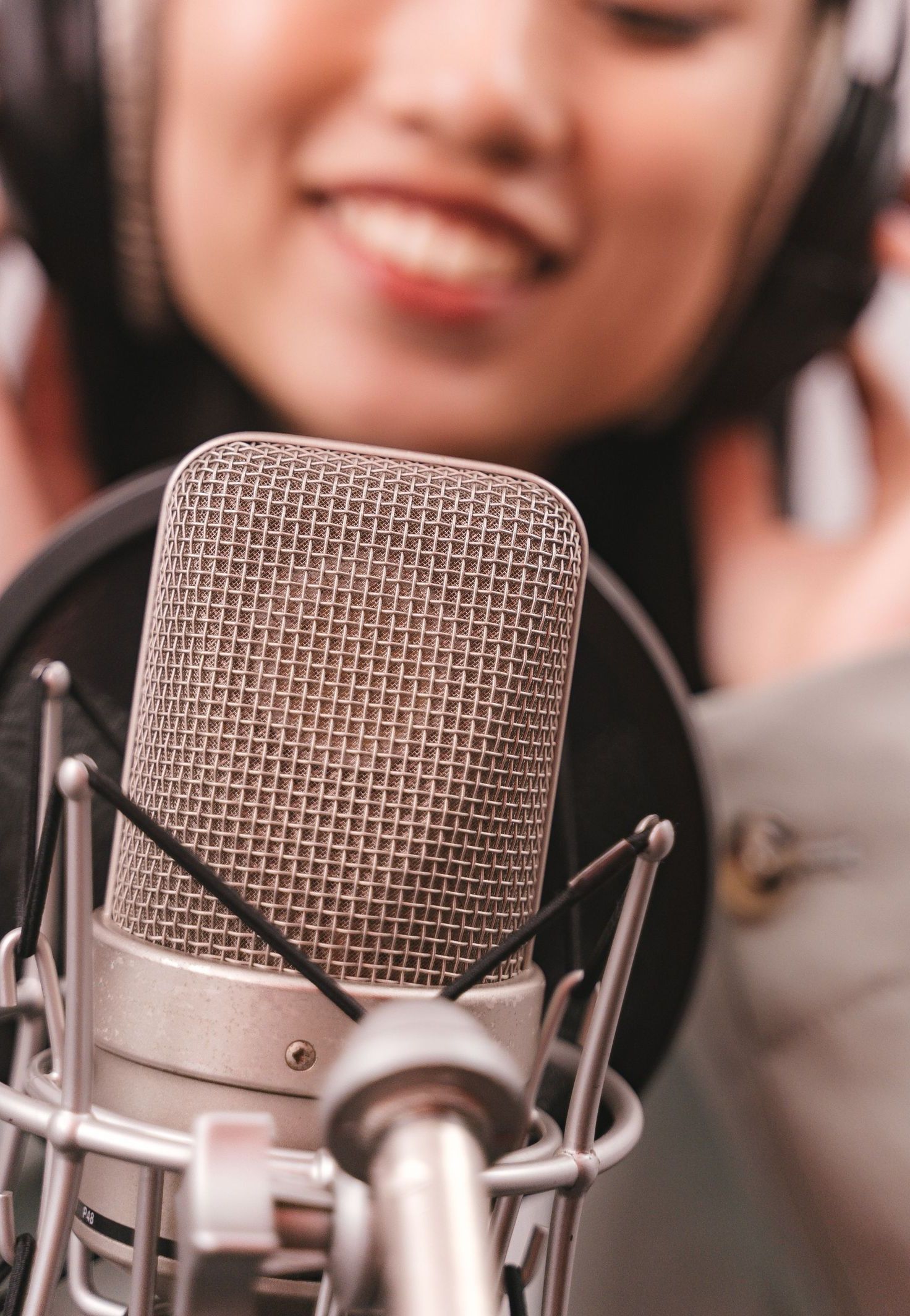 An Asian woman in a recording studio singing into a condenser microphone, wearing headphones.